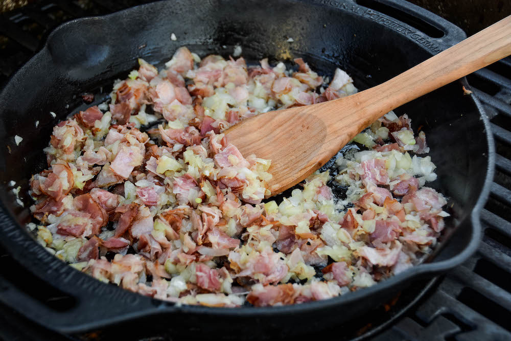 Zwiebel und Speck in der Feuerpfanne anrösten für die geräucherten Fleischbällchen in der Tomatensauce